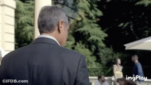 A Man In A Suit Is Standing In Front Of A Group Of People And A Sign That Says Imgplay On The Bottom GIF
