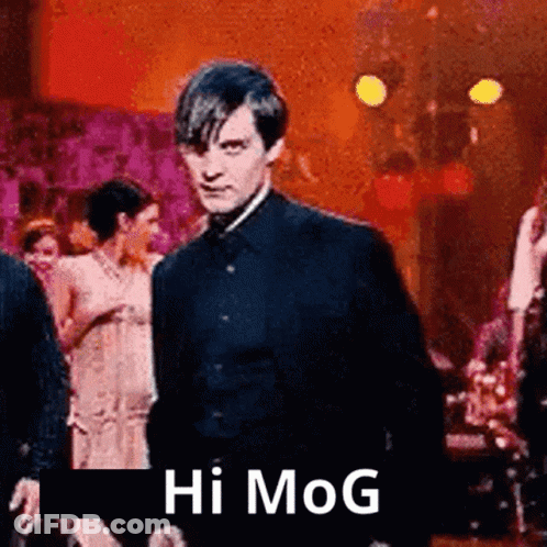 A Man In A Suit Is Standing In Front Of A Group Of People And Says Hi Mog . GIF