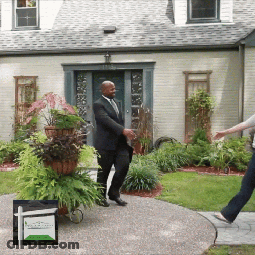 A Man In A Suit Is Standing In Front Of A House GIF