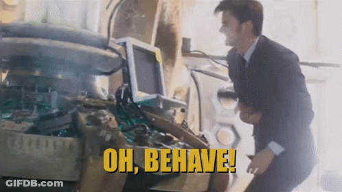 A Man In A Suit Is Standing In Front Of A Machine That Says " Oh Behave " GIF
