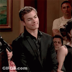 A Man In A Suit Is Standing In Front Of A Microphone In A Crowd . GIF