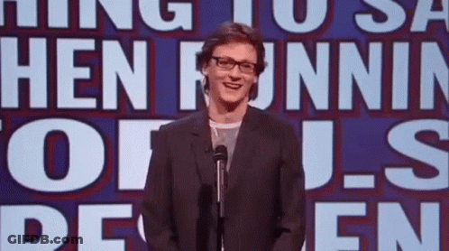 A Man In A Suit Is Standing In Front Of A Microphone In Front Of A Sign That Says Hen Funnin ' Of Us GIF