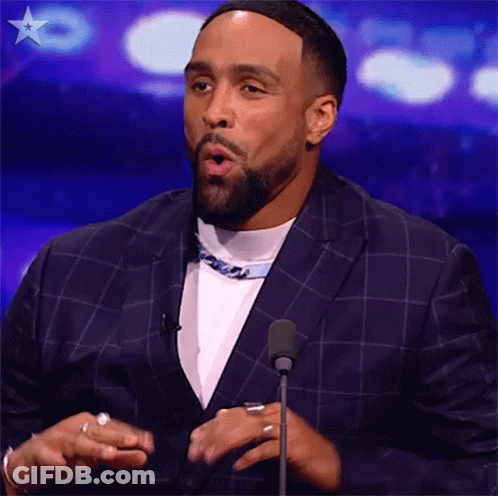 A Man In A Suit Is Standing In Front Of A Microphone . GIF