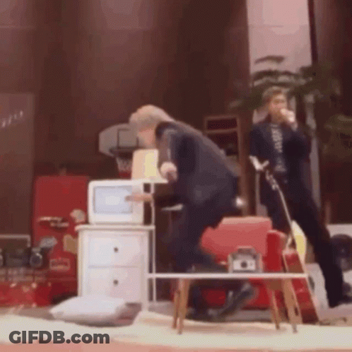 A Man In A Suit Is Standing In Front Of A Microwave In A Living Room GIF