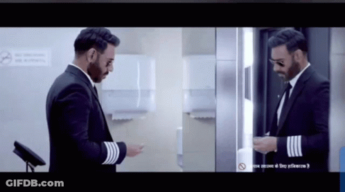 A Man In A Suit Is Standing In Front Of A Mirror GIF