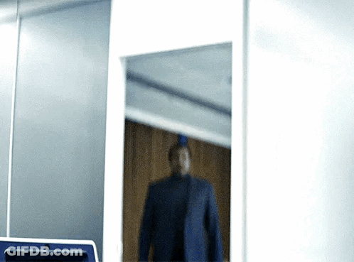 A Man In A Suit Is Standing In Front Of A Mirror In A Room GIF