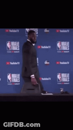 A Man In A Suit Is Standing In Front Of A Nba Finals Sign GIF