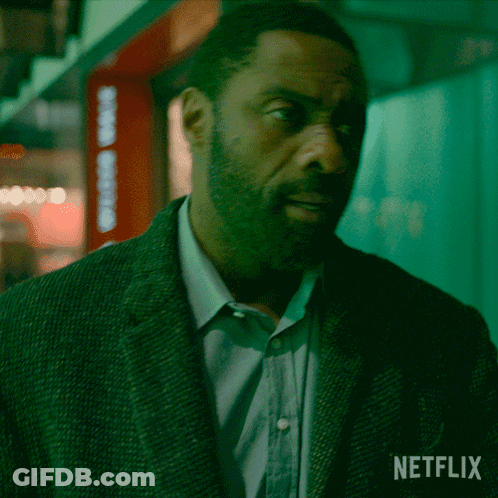 A Man In A Suit Is Standing In Front Of A Netflix Logo GIF