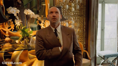 A Man In A Suit Is Standing In Front Of A Netflix Sign GIF