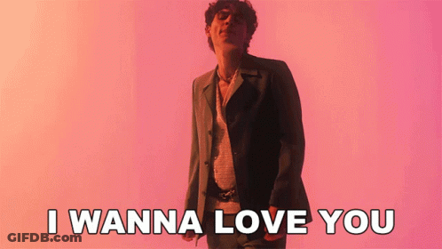 A Man In A Suit Is Standing In Front Of A Pink Background And Says I Wanna Love You GIF