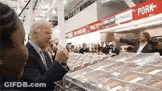 A Man In A Suit Is Standing In Front Of A Pork Section Of A Grocery Store GIF