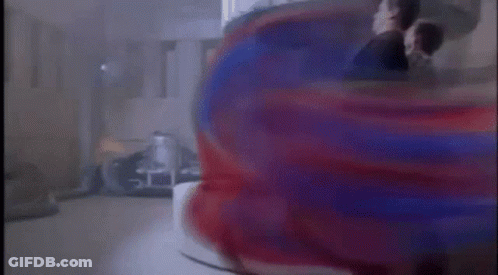 A Man In A Suit Is Standing In Front Of A Red And Blue Object In A Room . GIF