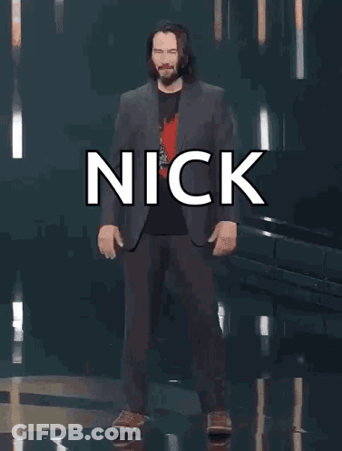 A Man In A Suit Is Standing In Front Of A Sign That Says Nick You 'Re Breathtaking ! GIF