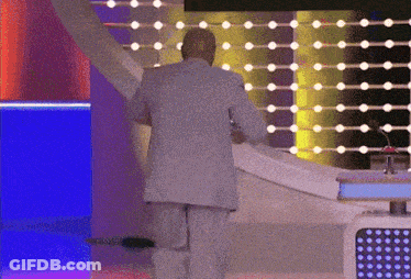 A Man In A Suit Is Standing In Front Of A Stage With Lights Behind Him GIF