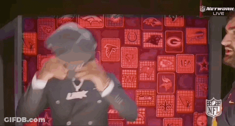 A Man In A Suit Is Standing In Front Of A Wall Of Nfl Logos . GIF