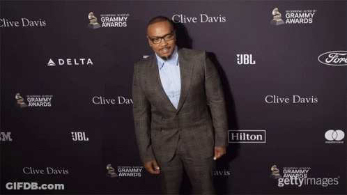 A Man In A Suit Is Standing In Front Of A Wall That Says Clive Davis On It GIF