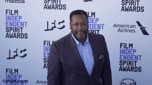 A Man In A Suit Is Standing In Front Of A Wall That Says Film Independent Spirit Awards GIF