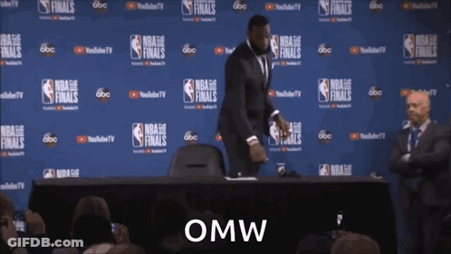 A Man In A Suit Is Standing In Front Of A Wall That Says Nba Finals GIF