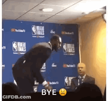 A Man In A Suit Is Standing In Front Of A Wall That Says Nba Finals On It . GIF