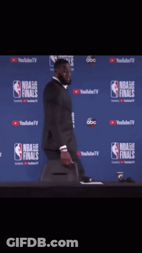 A Man In A Suit Is Standing In Front Of A Wall That Says Nba Finals On It GIF