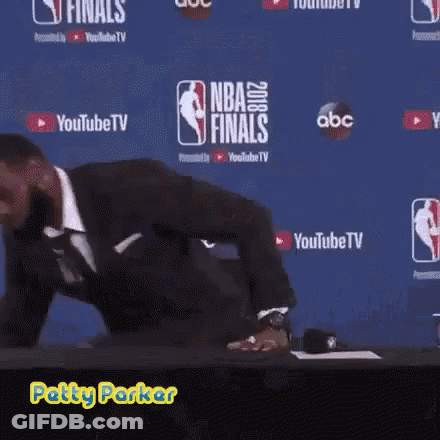 A Man In A Suit Is Standing In Front Of A Wall That Says Nba Finals On It GIF