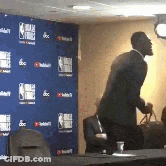 A Man In A Suit Is Standing In Front Of A Wall That Says Nba Finals On It GIF