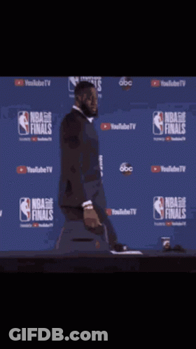 A Man In A Suit Is Standing In Front Of A Wall That Says Nba Finals On It GIF