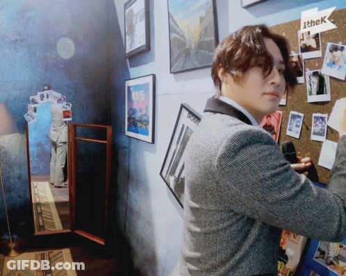 A Man In A Suit Is Standing In Front Of A Wall With Pictures On It And A Sign That Says Ithek GIF