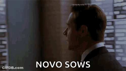 A Man In A Suit Is Standing In Front Of A Window With The Words Novo Sows Written On The Screen . GIF