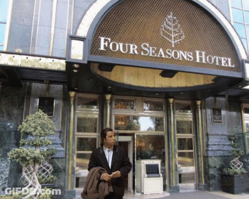 A Man In A Suit Is Standing In Front Of The Four Seasons Hotel GIF