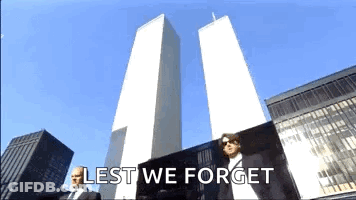 A Man In A Suit Is Standing In Front Of The Twin Towers With The Words Lest We Forget Written Below Him GIF