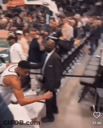 A Man In A Suit Is Standing Next To A Basketball Player In The Stands GIF