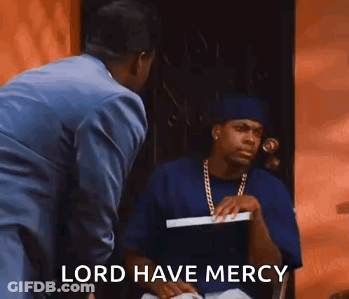 A Man In A Suit Is Standing Next To A Man In A Blue Shirt Who Is Sitting In Front Of A Door . GIF