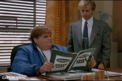 A Man In A Suit Is Standing Next To A Man Reading A Book Titled Brake Pads GIF