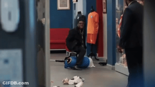 A Man In A Suit Is Standing Next To A Mannequin Wearing An Orange Shirt With The Letter B On It . GIF