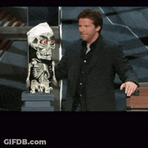 A Man In A Suit Is Standing Next To A Skeleton GIF