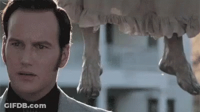 A Man In A Suit Is Standing Next To A Statue Of A Woman Hanging From A Building . GIF