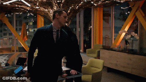 A Man In A Suit Is Standing Next To A Woman Holding A Tablet GIF