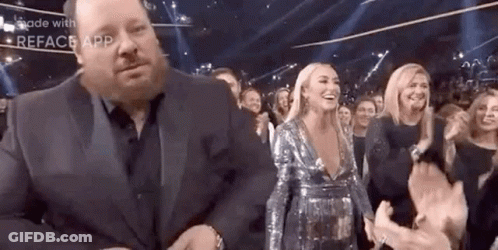A Man In A Suit Is Standing Next To A Woman In A Sequined Dress . GIF