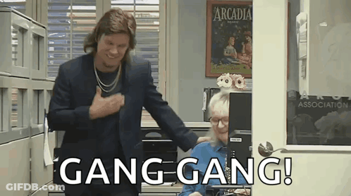 A Man In A Suit Is Standing Next To A Woman In An Office And Says Gang Gang ! GIF
