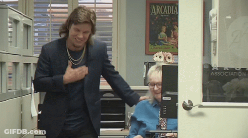 A Man In A Suit Is Standing Next To A Woman In Front Of A Computer With A Poster On The Wall That Says Arcadia GIF