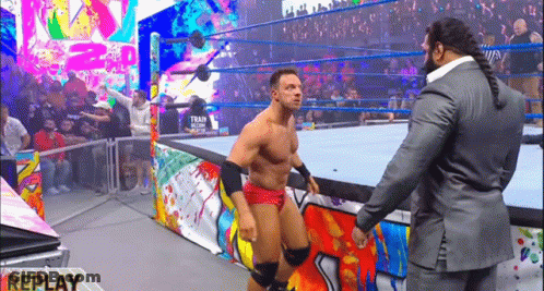 A Man In A Suit Is Standing Next To A Wrestler In A Ring . GIF