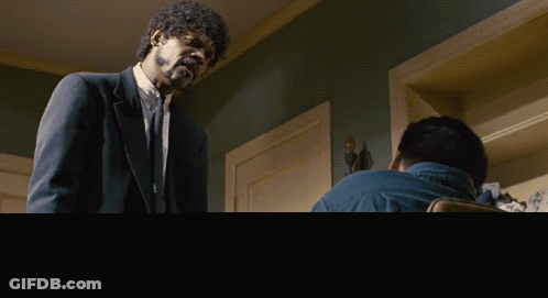 A Man In A Suit Is Standing Next To Another Man In A Chair GIF