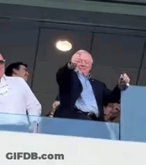 A Man In A Suit Is Standing On A Balcony Pointing At The Camera . GIF