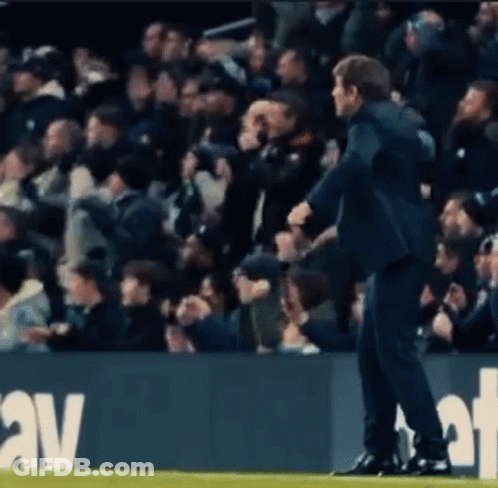 A Man In A Suit Is Standing On A Soccer Field In Front Of A Crowd Of People . GIF