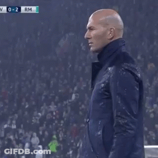 A Man In A Suit Is Standing On A Soccer Field With His Hand On His Forehead . GIF