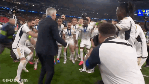 A Man In A Suit Is Surrounded By A Group Of Soccer Players Including One With The Number 2 On His Shirt GIF