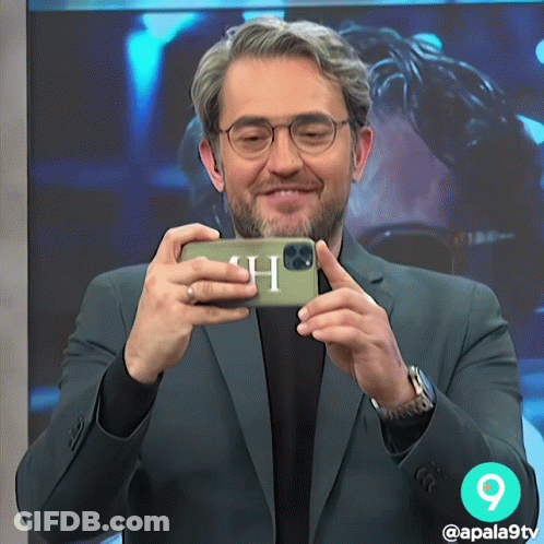 A Man In A Suit Is Taking A Picture Of Himself With A Phone With The Letter H On It GIF