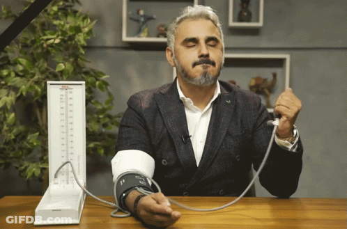 A Man In A Suit Is Taking His Blood Pressure With A Device That Says Tcm GIF