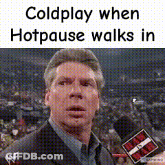 A Man In A Suit Is Talking Into A Microphone While A Crowd Watches . GIF